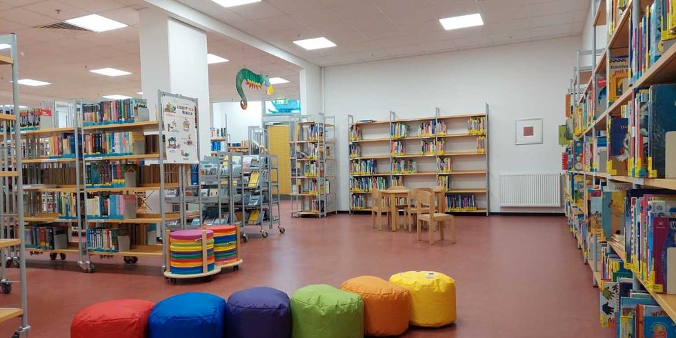 fünf bunte Hocker vor Regalen, gefüllt mit Kinderbüchern