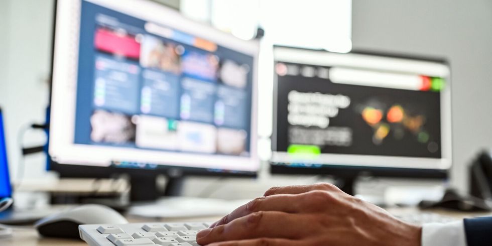 Hand an Computertastatur vor Monitoren mit IT- und Sicherheitsanzeigen