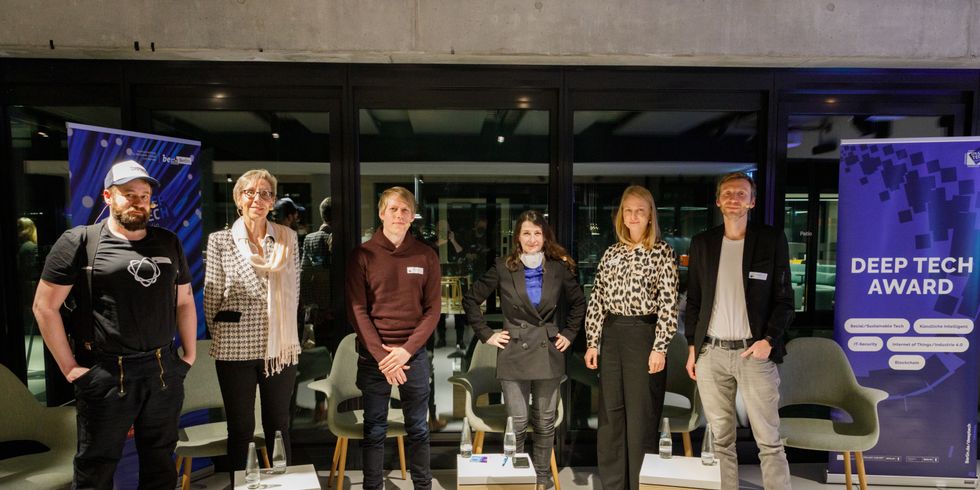 Die Panelist:innen und die Moderatorin stehen vor einer Glaswand