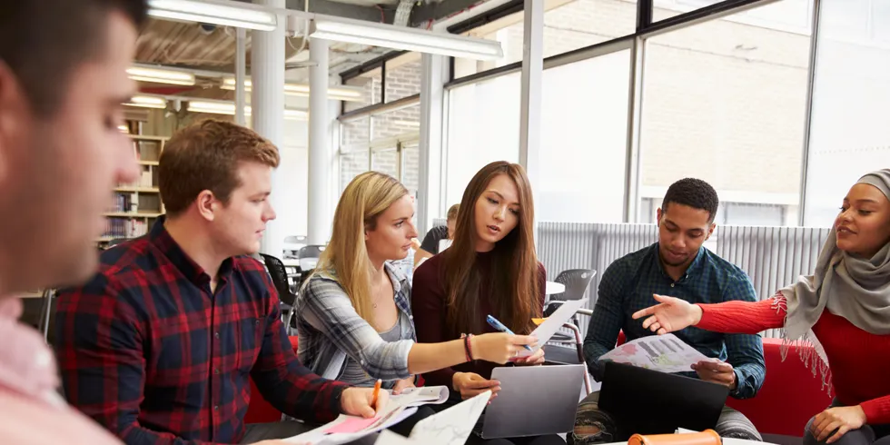 Gruppe Studenten sitzt an einem runden Tisch und macht Projektarbeit