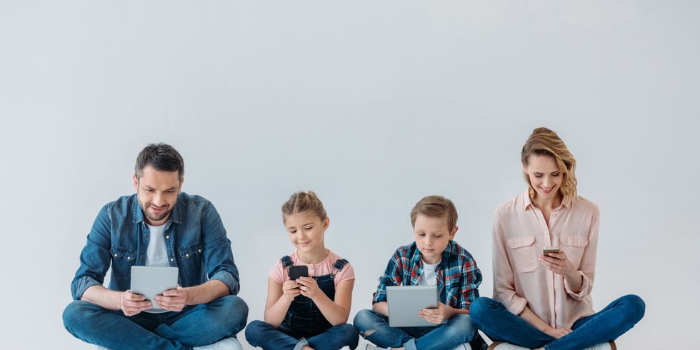 Eltern mit zwei Kindern sitzen auf dem Boden und halten jeweils ein Handy oder ein Tablet
