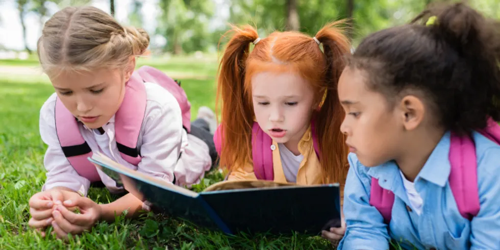 Drei Kinder lesen im Park auf der Wiese gemeinsam ein Buch
