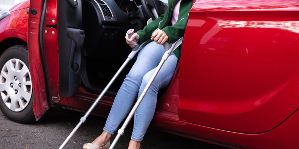 eine Frau auf Krücken steigt aus einem Auto