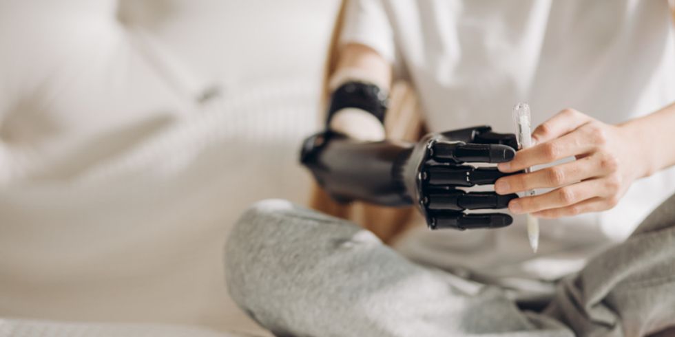 Frau hält mit beiden Händen einen Stift, sie trägt rechts eine Armprothese