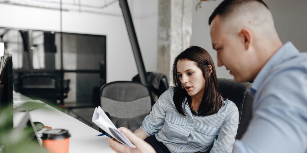Zwei Personen, Frau und Mann, in Bürokleidung arbeiten gemeinsam am Schreibtisch sitzend mit Dokumenten in einem hellen, modernen Büro