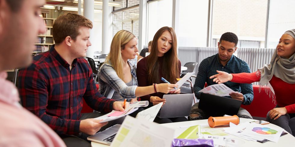 Gruppe Studenten sitzt an einem runden Tisch und macht Projektarbeit