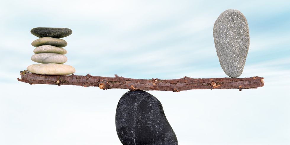 Auf einem Stein liegt ein Ast. Auf der linken Seite liegen mehrere flache Steine übereinander auf dem Ast. Auf der rechten Seite hält ein größerer Stein das Gleichgewicht.