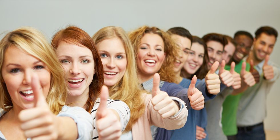 Jungen Menschen stehen hintereinander in einer Reihe und halten ihren linken Daumen hoch