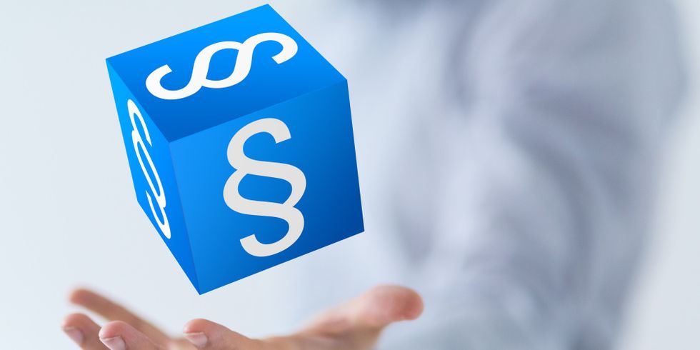 Blauer Würfel mit Paragraphen schwebend über einer Hand