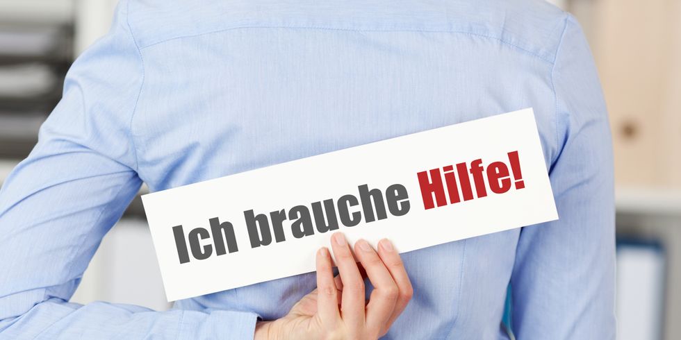 Eine Frau hält hinter ihrem Rücken ein Schild mit der Aufschrift 'Ich brauche Hilfe'
