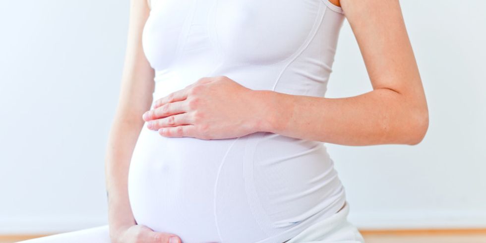 Schwangere Frau umfasst ihren Bauch mit den Händen