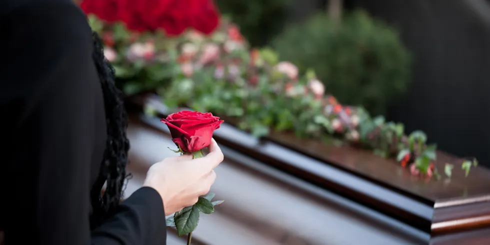 Frau steht auf einer Beerdigung mit Rose in der Hand vor einem Sarg