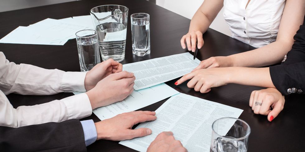 Verschiedene Schriftstücke liegen auf einem Tisch und werden von mehreren Personen diskutiert
