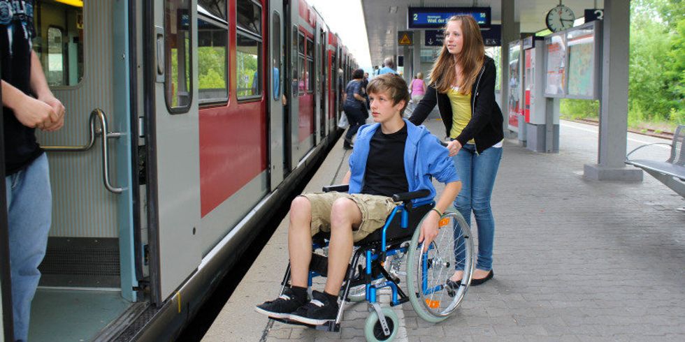 Mädchen schiebt Teenager im Rollstuhl Richtung wartendem Zug am Bahnsteig