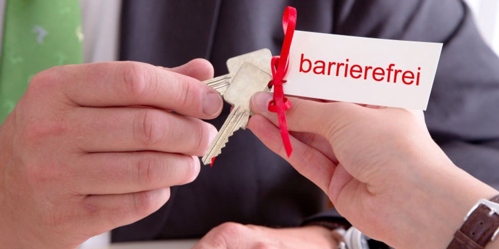 Ein Schlüsselbund mit einem Schild mit der Aufschrift 'barrierefrei' wird einem Mann überrreicht