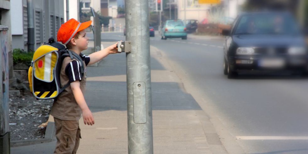 kleiner Schuljunge steht an einer Ampel um die Straße zu überqueren