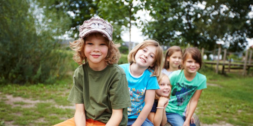 Das Bild zeigt fünf Kinder die auf einem Baumstamm sitzen