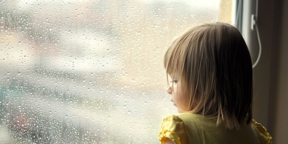 Kind stehend am verregnetem Fenster