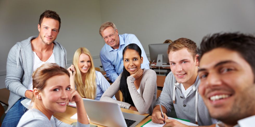 Gruppe von Studenten um einen Tisch mit Lernmaterialien lacht in die Kamera