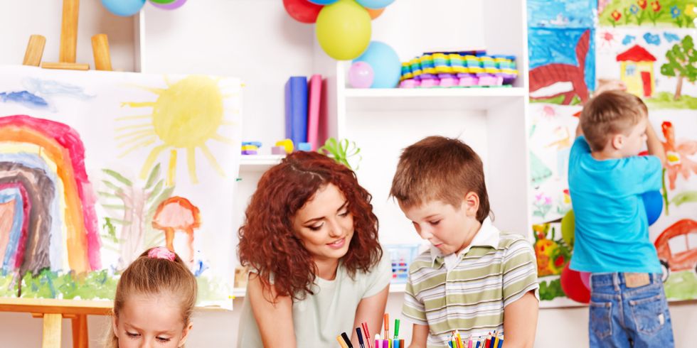 Das Bild zeigt eine Erzieherin und drei Kindern beim Basteln in einem Aufenthaltsraum