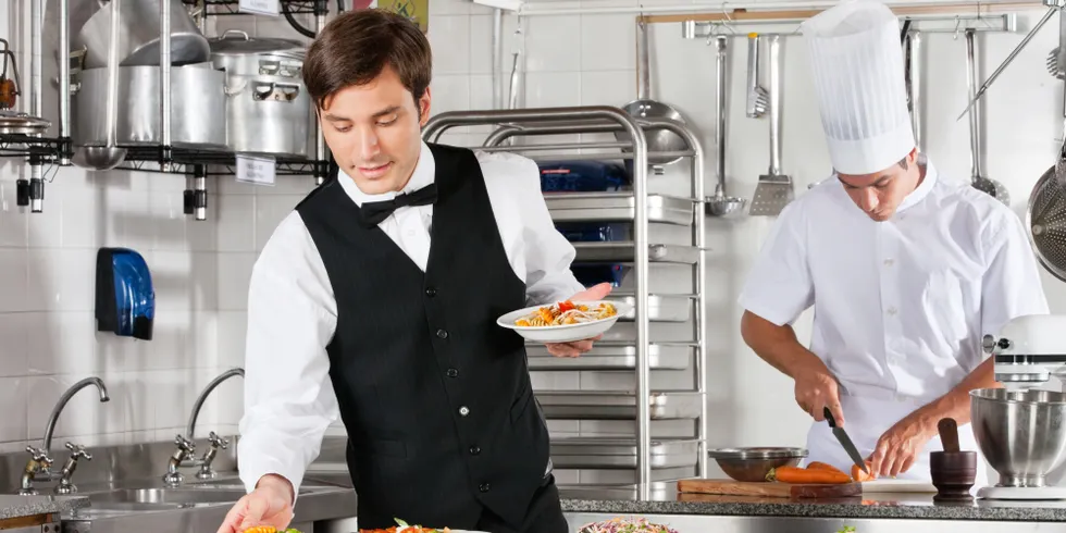 Kellner und Chefkoch beim Arbeiten in einer kommerziellen Küche