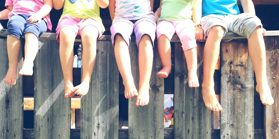 Kinderbeine bäumeln über einem Zaun