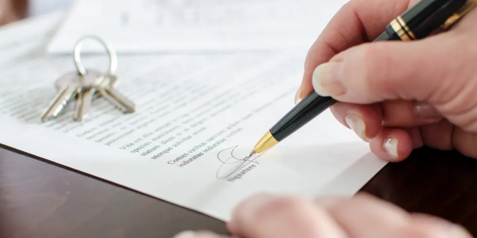 Eine Person unterschreibt ein Schriftstück, auf dem Blatt Papier liegt ein kleines Schlüsselbund
