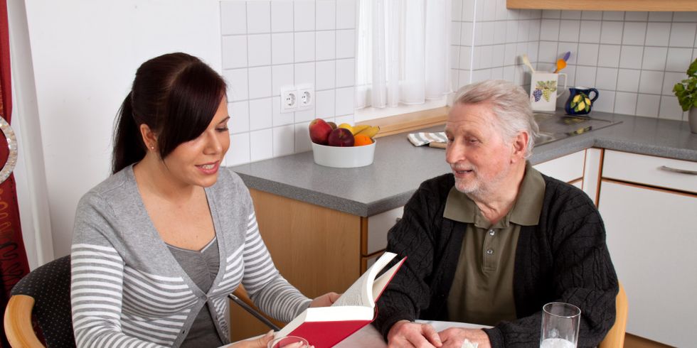 Junge Frau liest in einer Küche Senior aus Buch vor