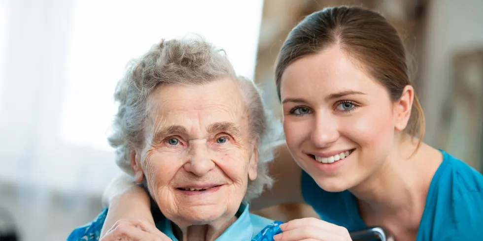 Junge Pflegerin umarmt lächelnde Seniorin