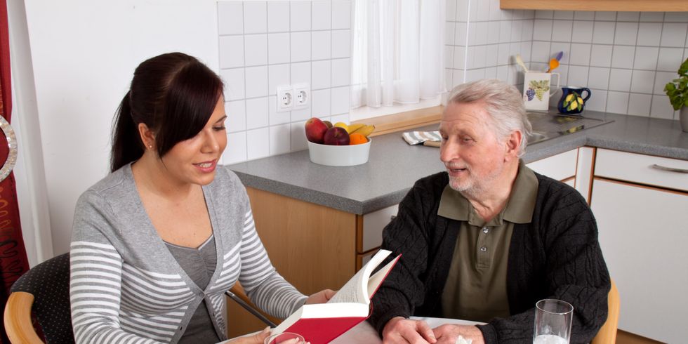 Junge Frau liest in einer Küche Senior aus Buch vor
