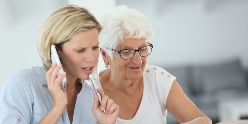 Seniorin zeigt auf eine Seite in einem Terminkalender, eine junge Frau sitzt daneben und telefoniert