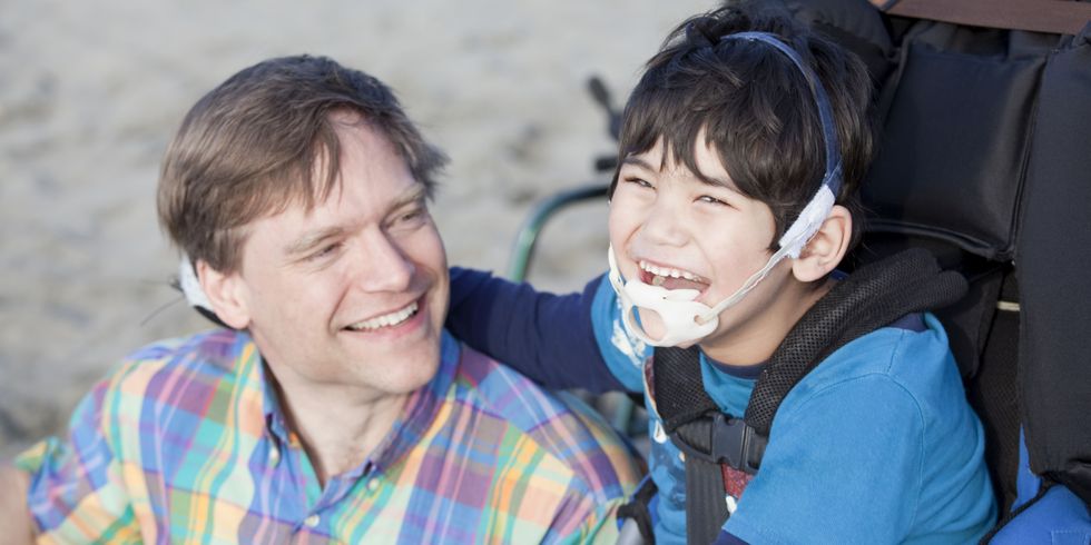 Ein Vater sitzt lächelnd neben seinem behinderten Sohn am Strand