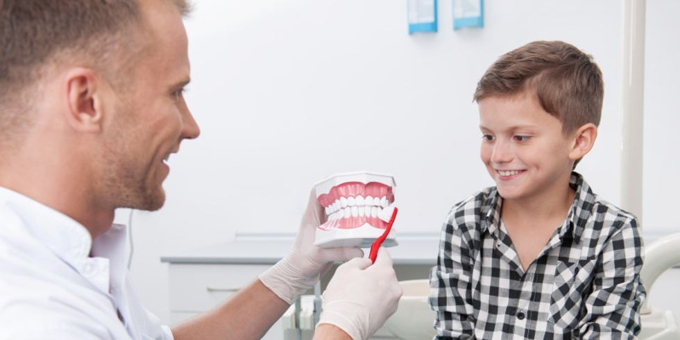 Zahnarzt erklärt Jungen anhand eines Modells die richtige Zahnpflege