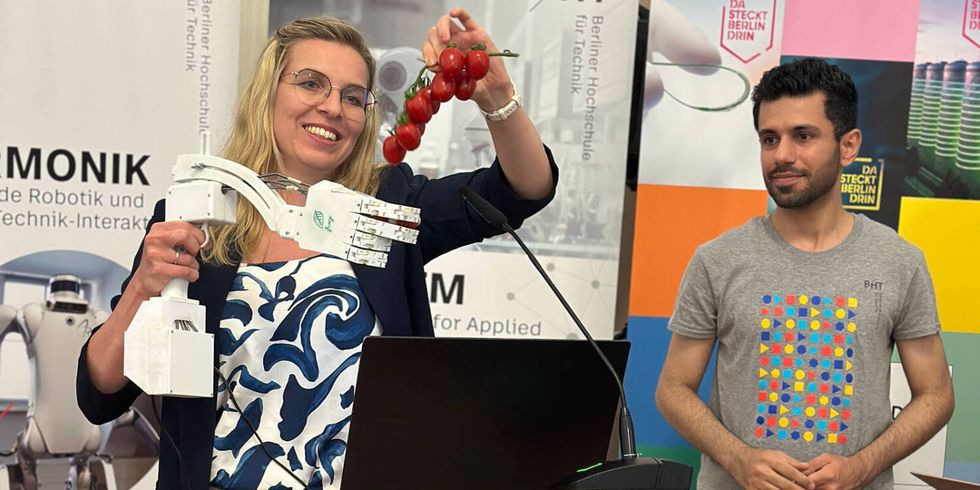 Eine Frau präsentiert eine Roboterhand die nach Tomaten greift