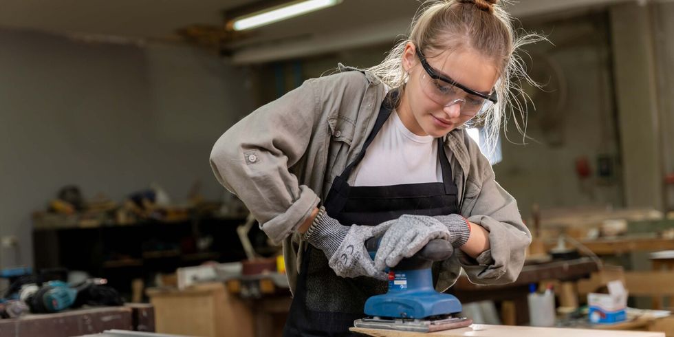 Eine junge Frau schleift in einer Werkstatt ein Holzstück ab.