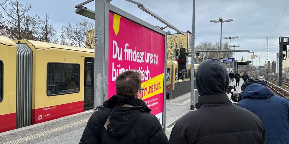 S-Bahn steht hinter Kampagnenplakat am S-Bahnhof.