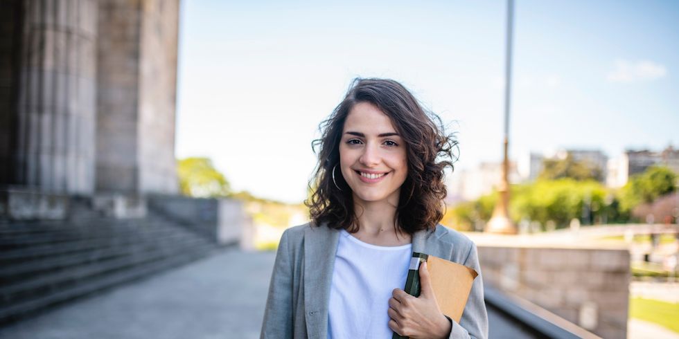 Frau mit Buch vor einem Universitätsgebäude