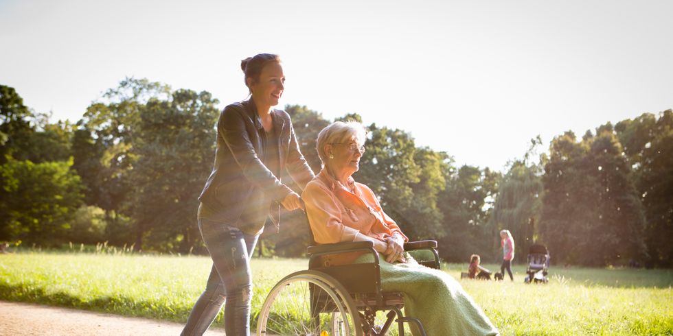 Junge Frage schiebt eine Seniorin in einem Rollstuhl durch einen Park