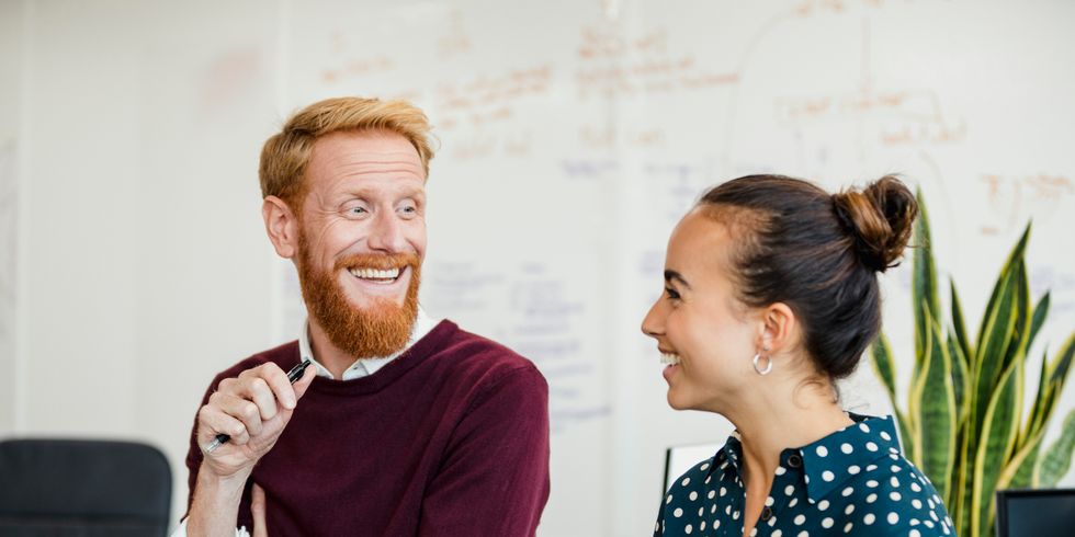 Eine junge Frau und ein junger Mann sprechen und lachen miteinander im Büro.