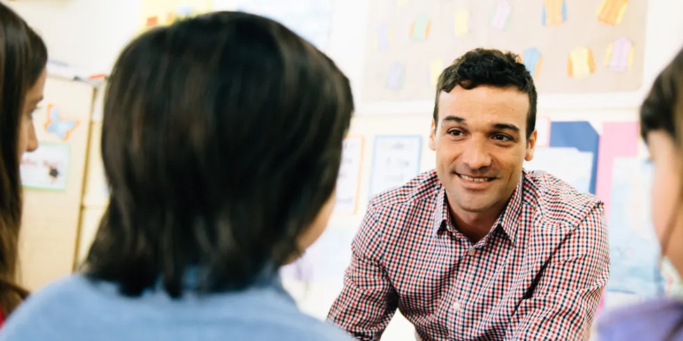 Ein Lehrer sitzt drei Schülerinnen gegenüber und spricht