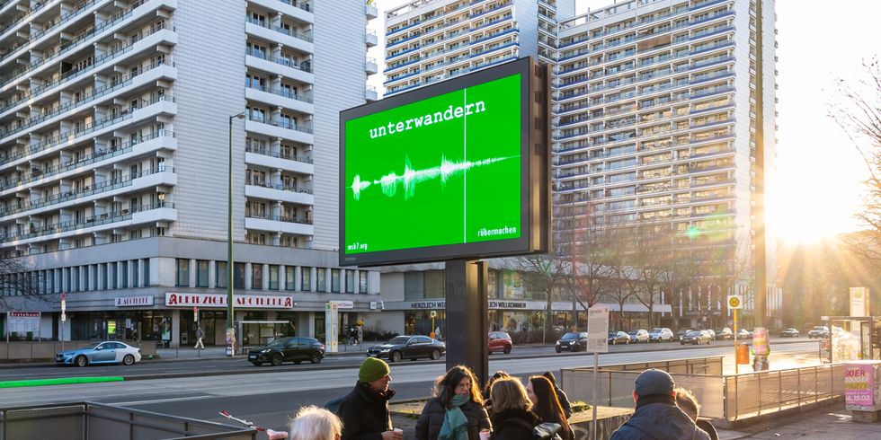 Straße in der Abendsonne mit grüner Werbetafel, darauf steht "unterwandern"