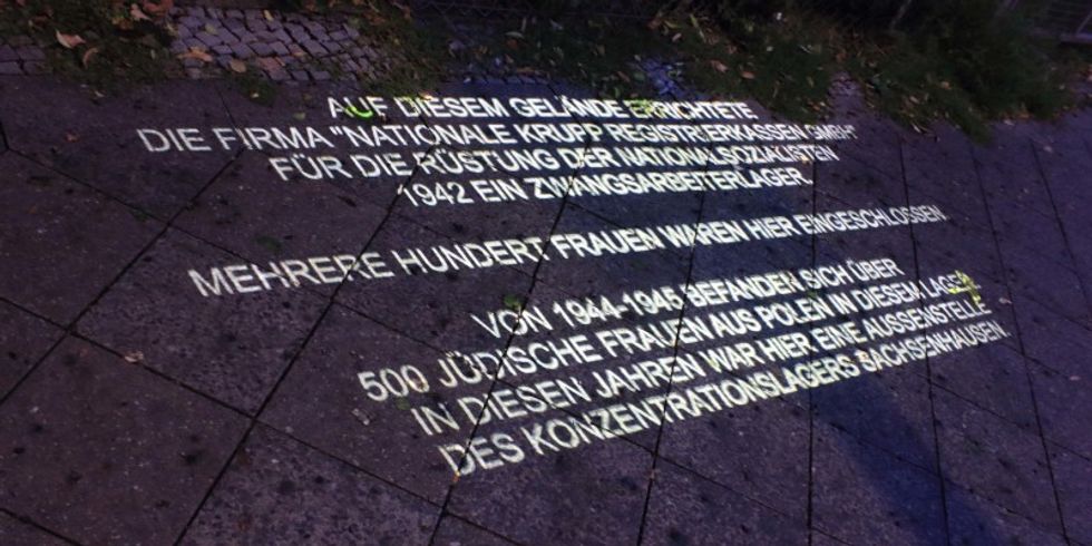 Lichtschriftprojektion auf die Straße Sonnenallee mit Angaben zum Zwangsarbeiterlager