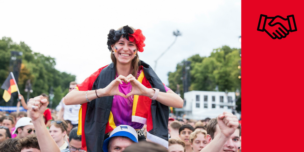Header für das Thema "Gesellschaftliche Unterstützung" - Menschen auf der Fanmeile. Eine Frau formt mit ihren Händen ein Herz.
