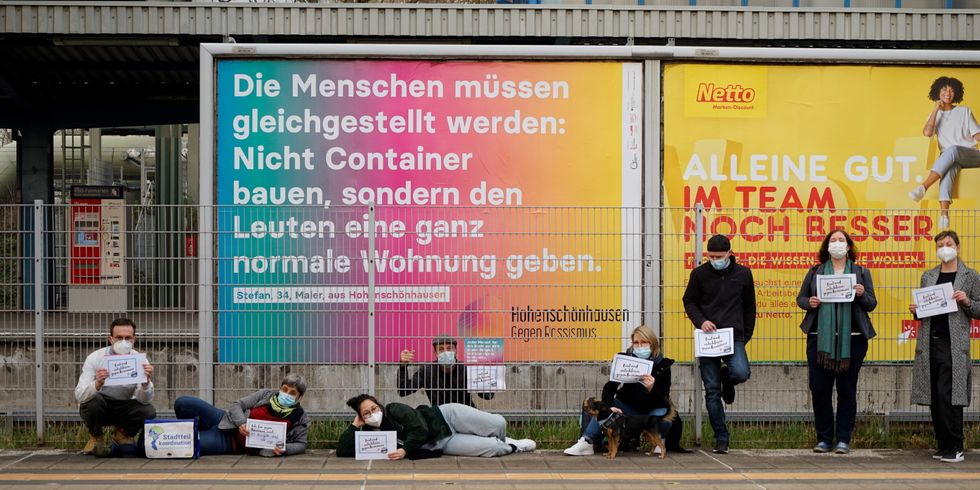 Menschen demonstrieren vor Plakatwand gegen Rassismus