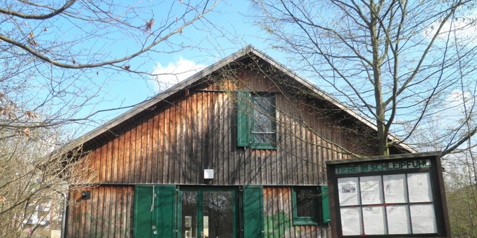 Eingangsbereich mit Gebäude aus Holz und Hinweisschild