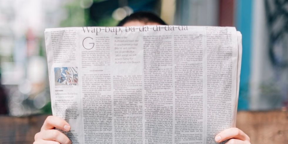 Ein Mann sitzt auf einer Bank und liest eine Zeitung.