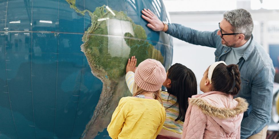 Lehrer steht mit Schülerinnen vor großen Globus