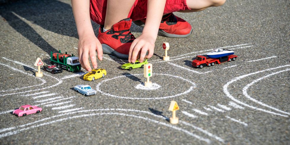 Junge spielt mit Modellautos auf einer Straße, dort ist mit Kreide ein Kreisverkehr aufgemalt