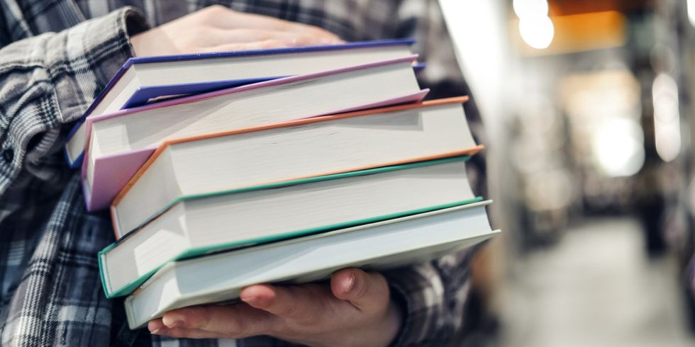 Mädchen hält einen Stampel Bücher vor ihrem Bauch - Bildausschnitt vom Oberkörper