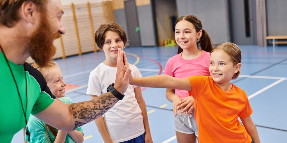 Gruppe junger Kinder steht begeistert in einer Turnhalle und klatschen mit dem Lehrer ein